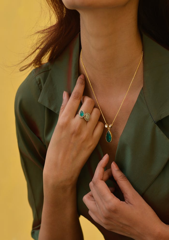 Close-up of a woman showcasing elegant emerald necklace and ring against a yellow background.