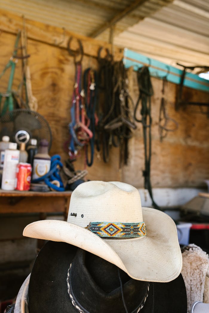 Close-up of a cowboy hat with beaded band in a rustic tack room, showcasing western lifestyle.